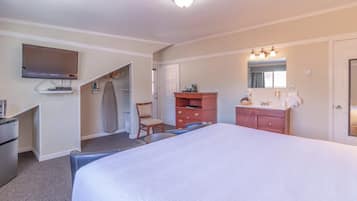 A hotel room with a large bed, a TV mounted on the wall, a desk with a chair, a wardrobe, and a bathroom with a mirror and sink.