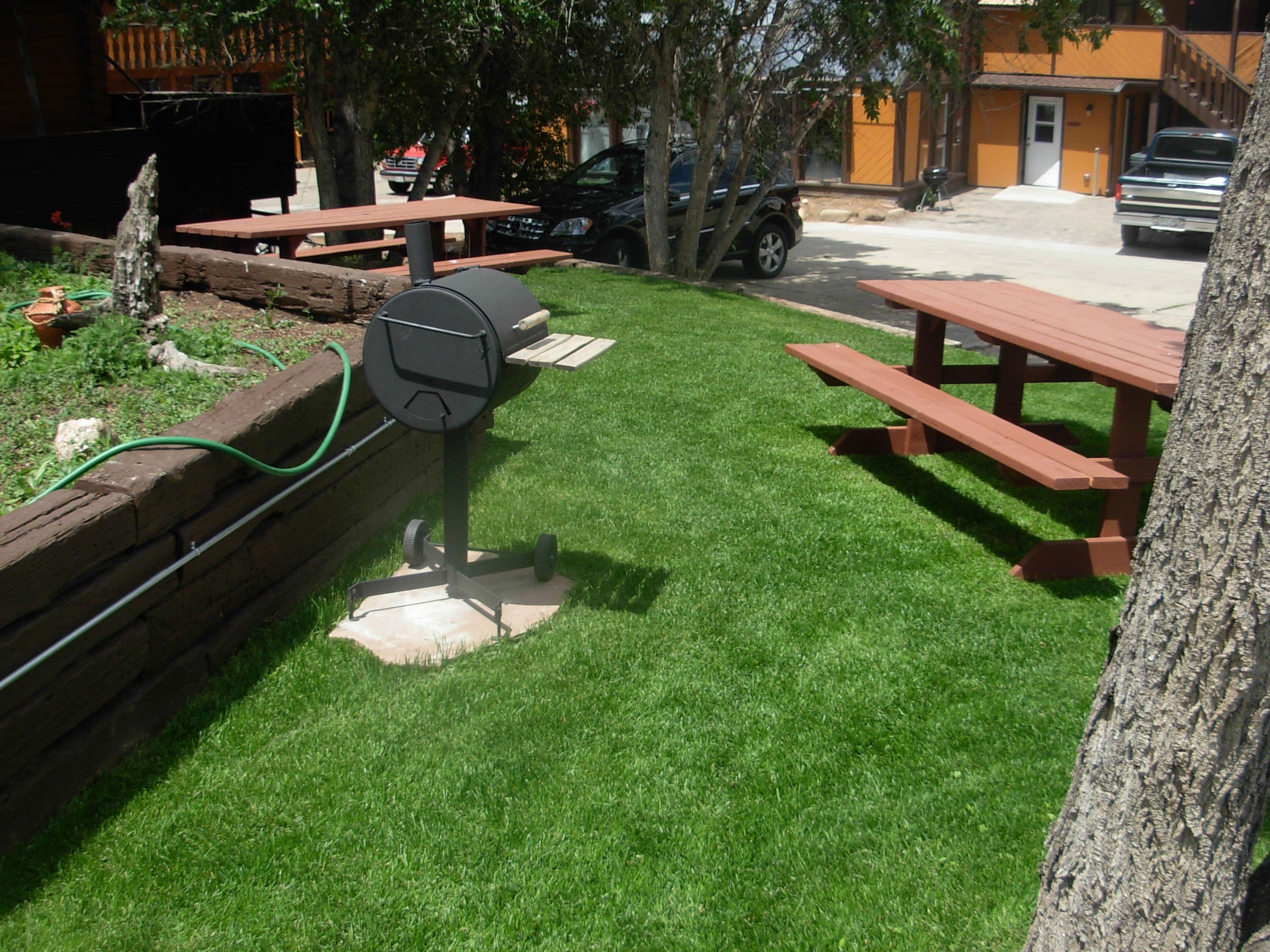 Un espace herbeux équipé de tables de pique-nique et d’un barbecue.