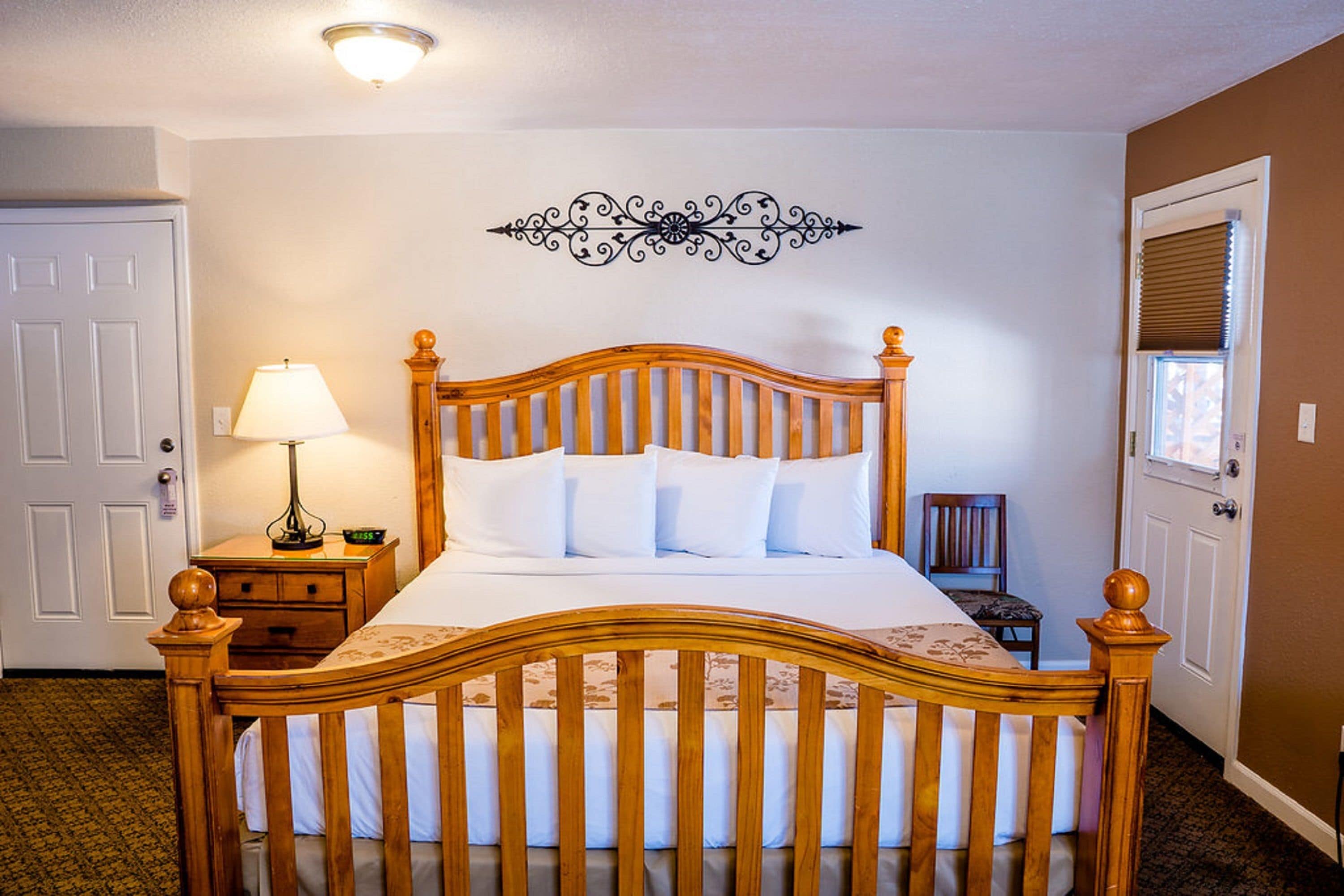 Un letto ben rifatto con una testiera in legno, una lampada da comodino e un elemento decorativo appeso sopra.