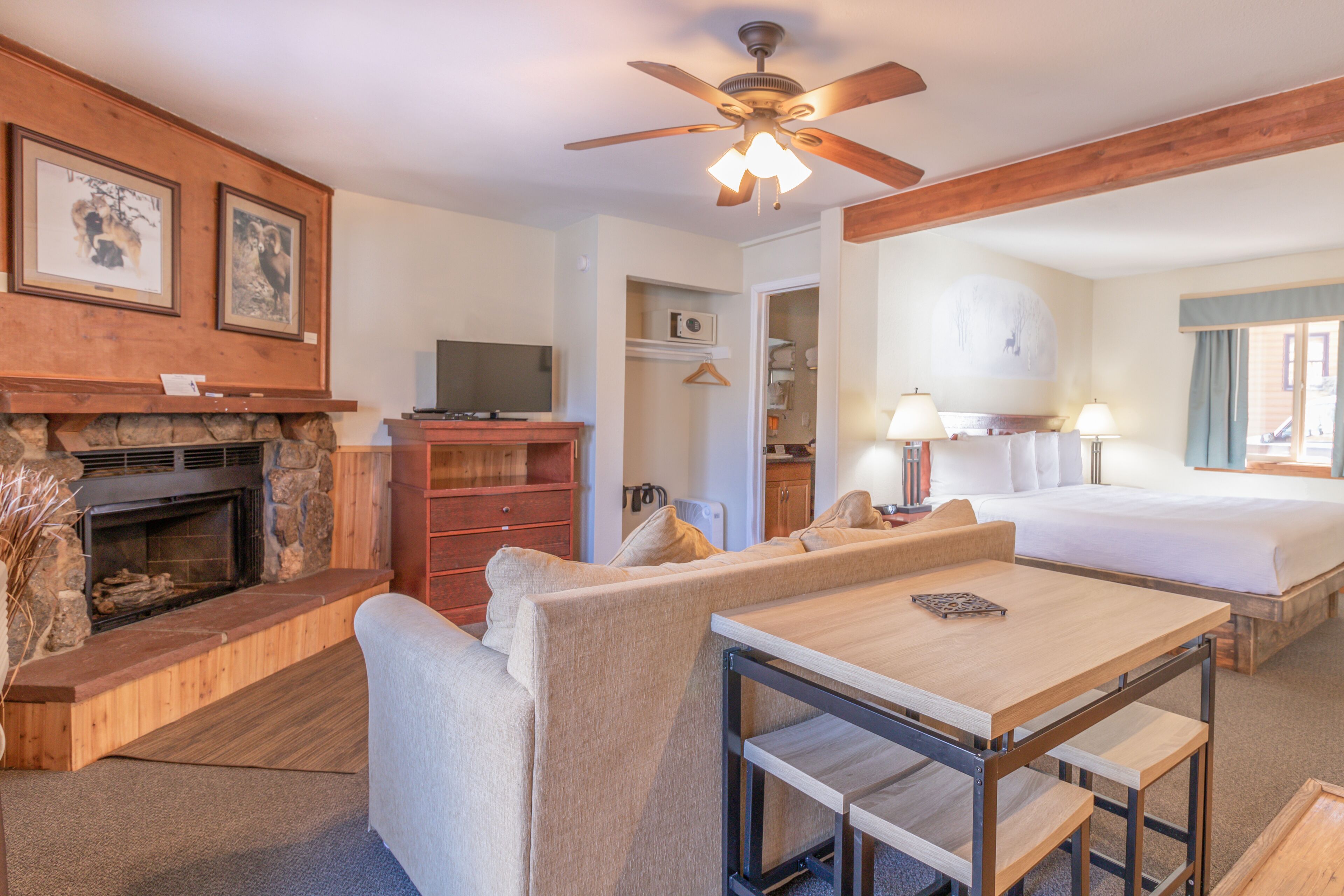 A hotel room with a fireplace, a sofa, a bed, a desk, and a ceiling fan.