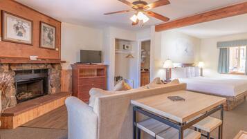 A hotel room with a fireplace, a sofa, a bed, a desk, and a ceiling fan.