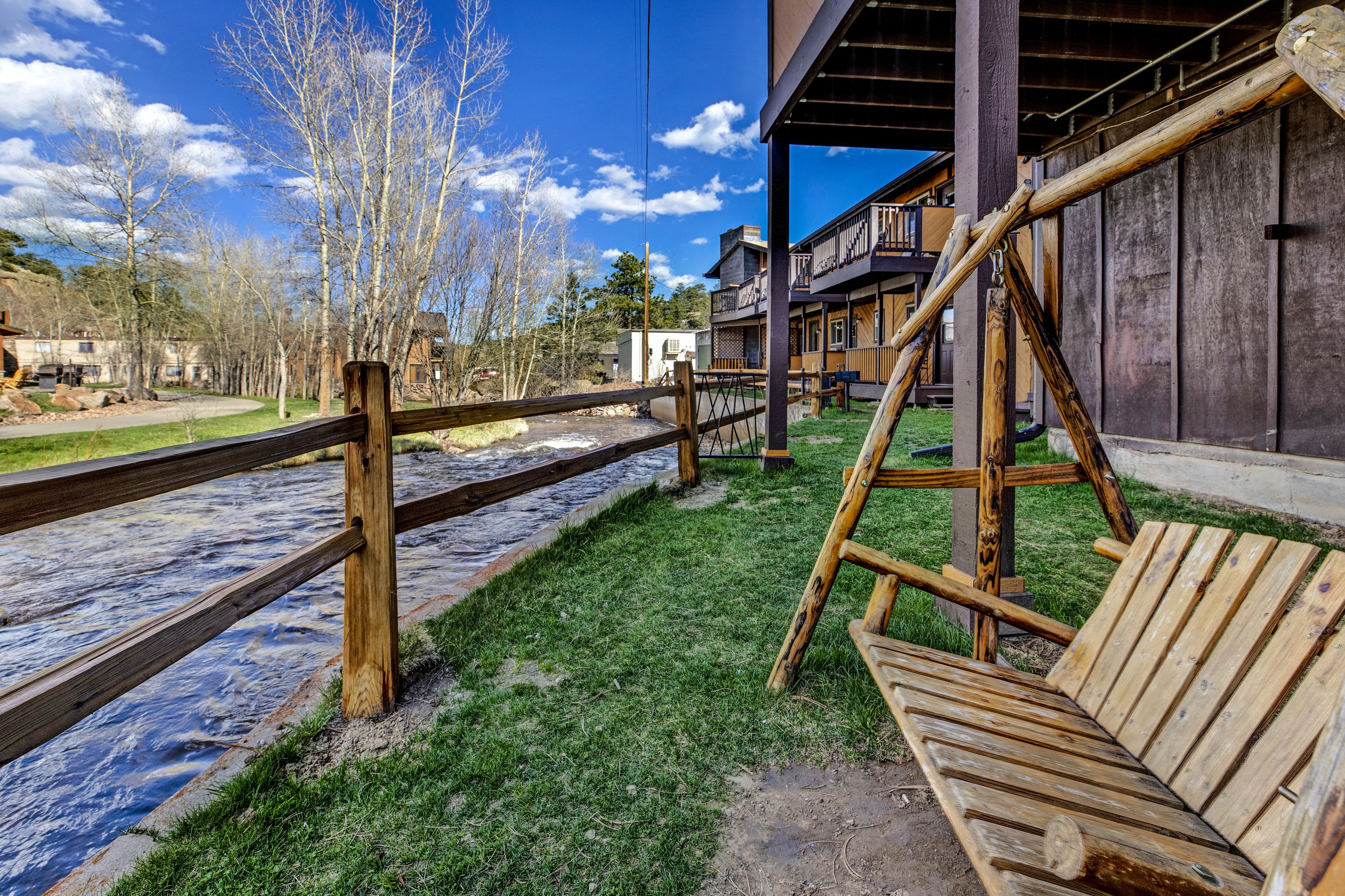 A wooden deck with a bench, a wooden fence, and a view of a river and buildings in the background.