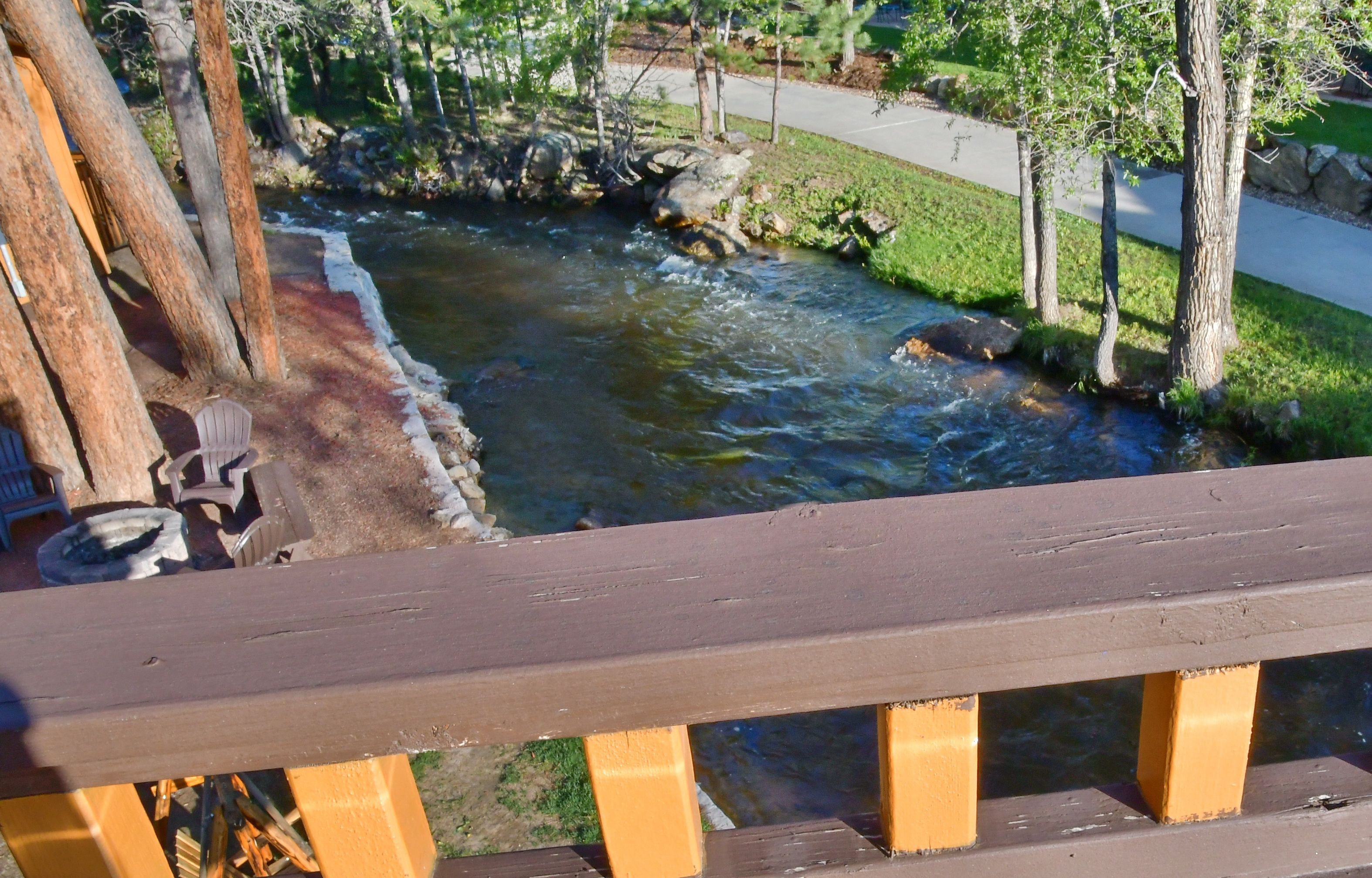 A wooden deck overlooking a small stream with rocks and trees.