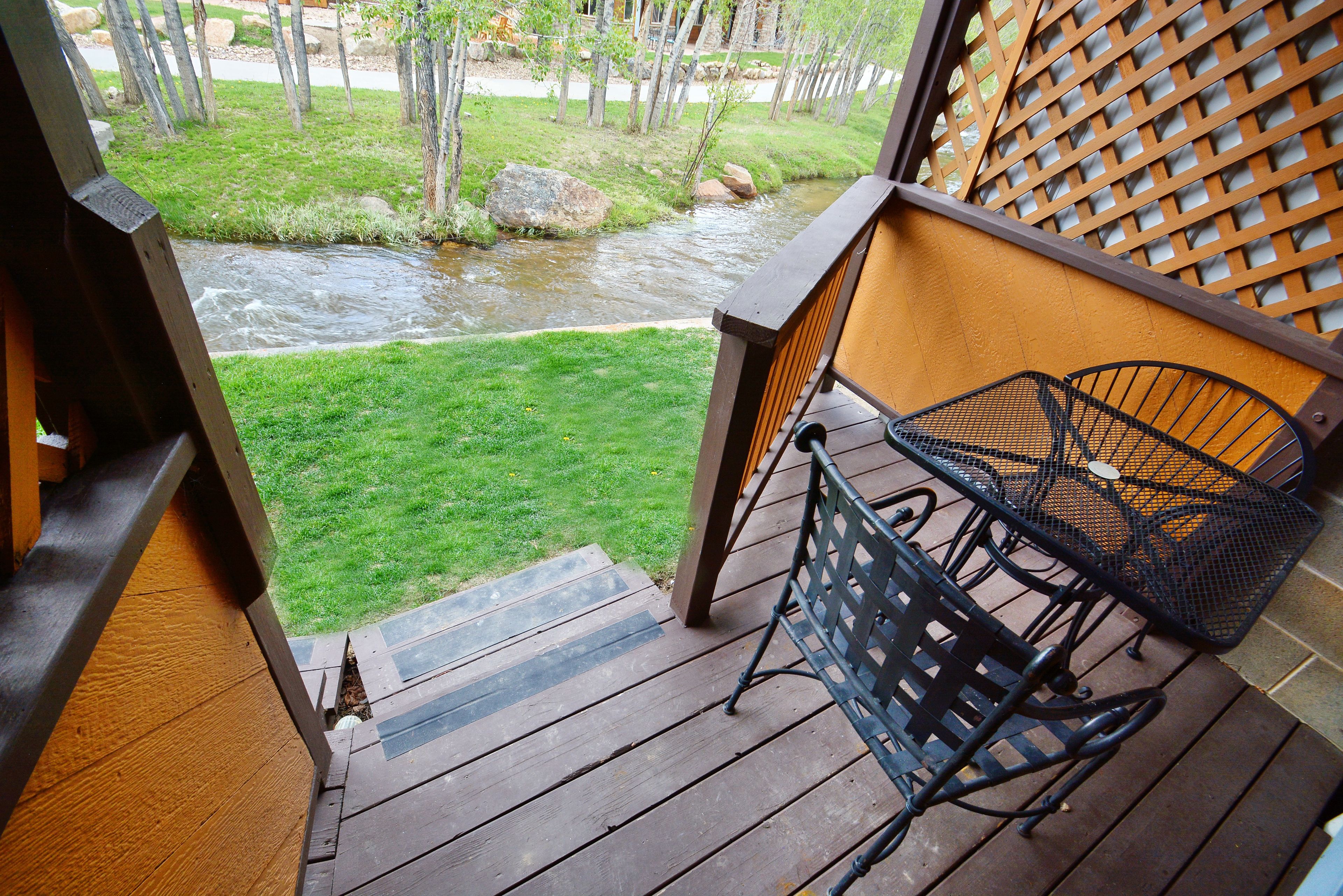 A wooden deck with a metal chair and a view of a stream.