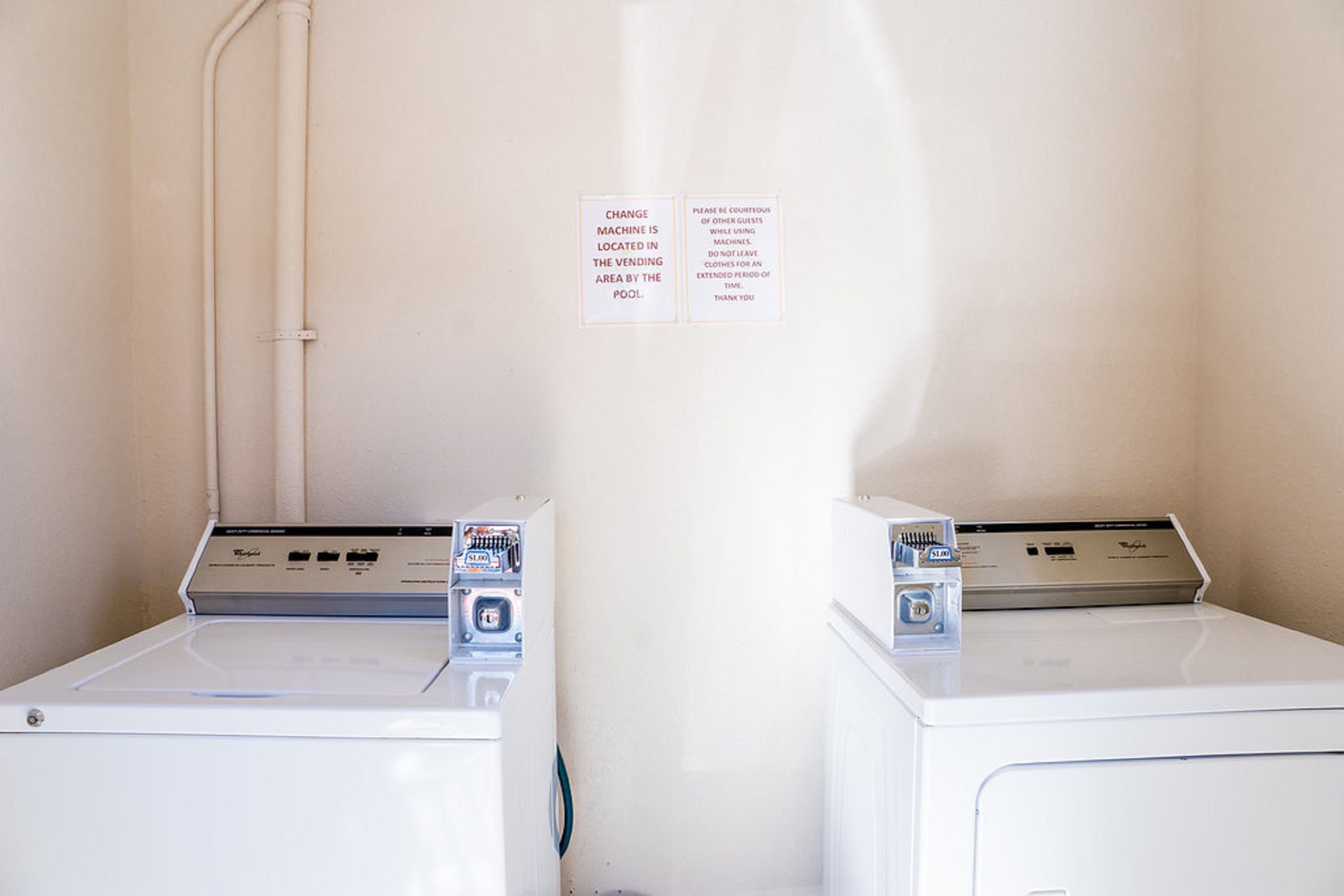A laundry room with two white washing machines and a sign indicating the location of the change machine.