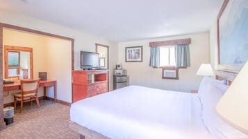 Habitació d'hotel amb un llit gran, un escriptori amb un ordinador, televisió i un frigorífic petit.