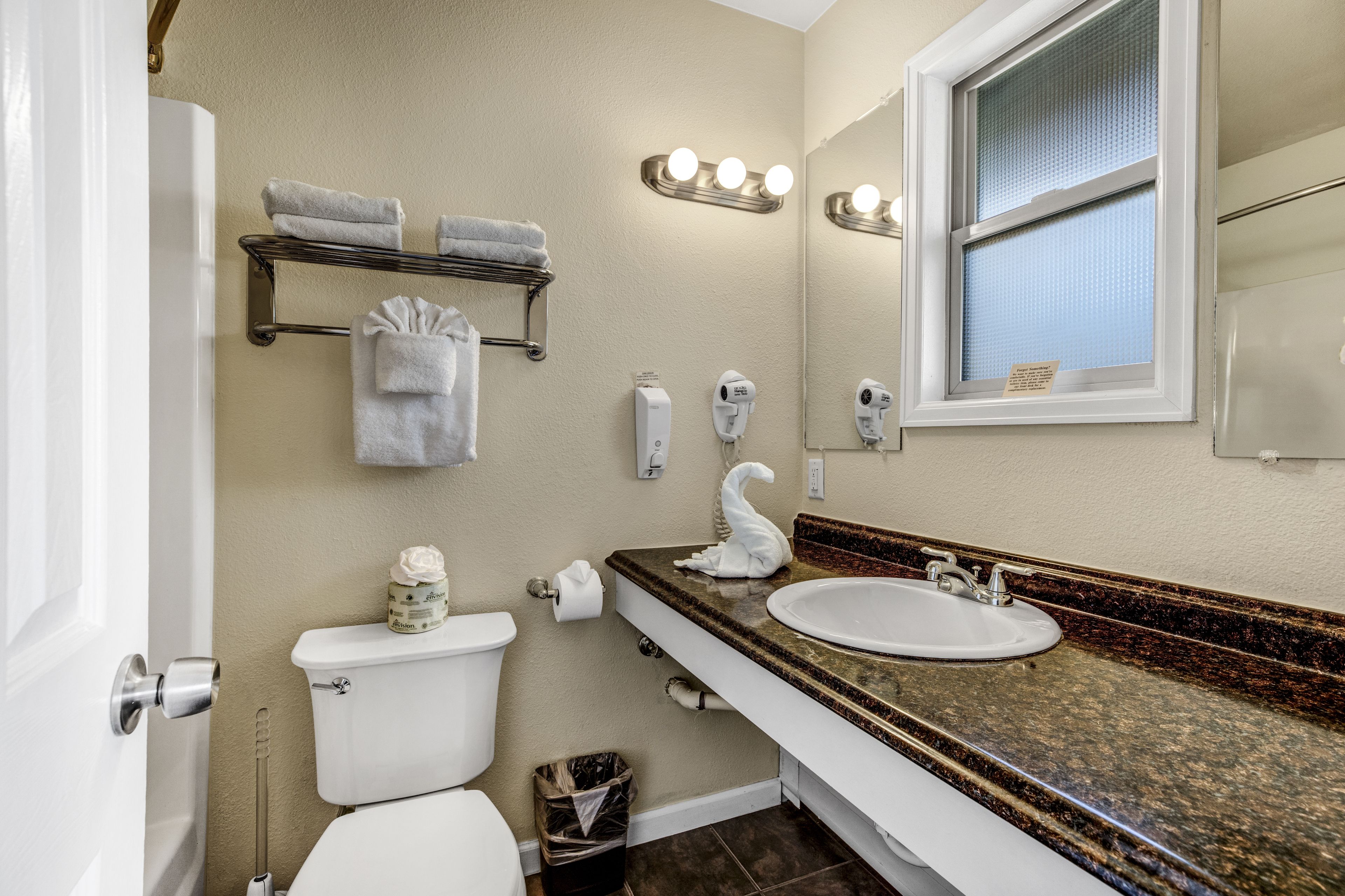 A bathroom with a toilet, sink, vanity, towel rack, and a window with blinds.