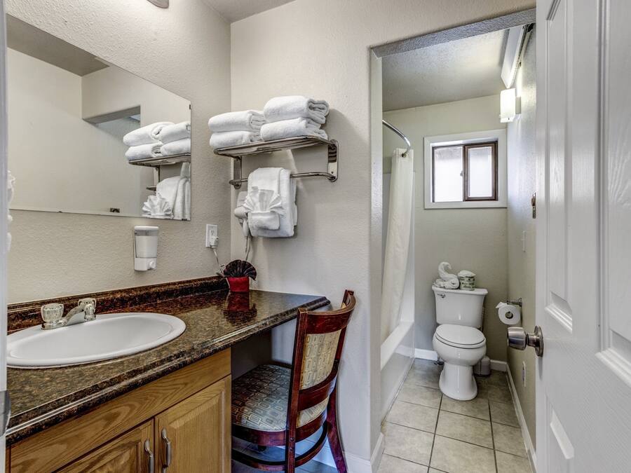 A bathroom with a sink, mirror, towel rack, toilet, and shower area.