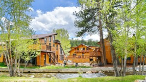A lodge with multiple wooden buildings, outdoor seating, and a stream. - Murphy's River Lodge (Estes Park)