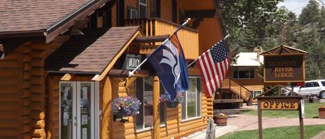 Una cabana de fusta amb un porxo, una bandera dels Estats Units i un rètol que indica l'oficina de Murphy's River Lodge.