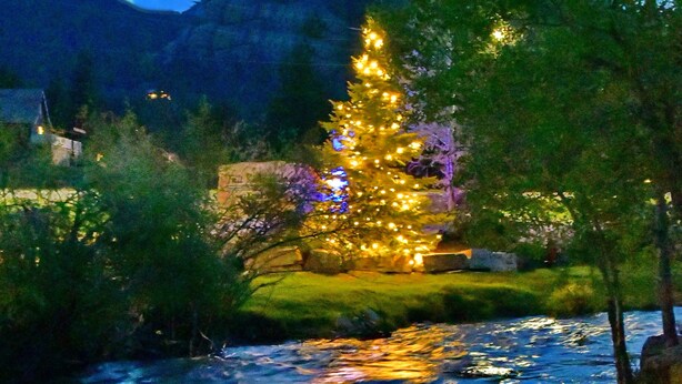 A river with a Christmas tree decorated with lights. - Murphy's River Lodge (Estes Park)