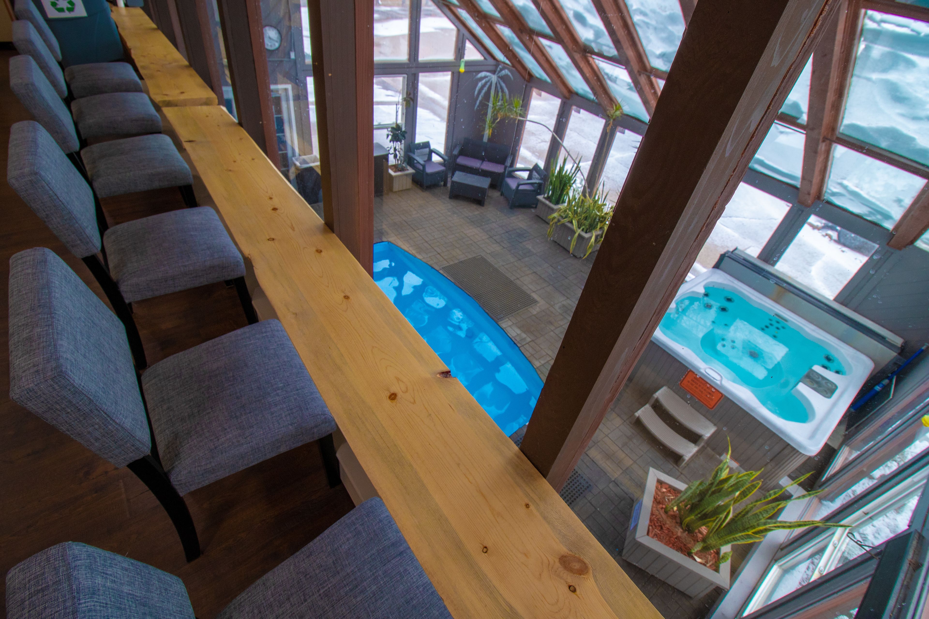 A long wooden bench with grey upholstered chairs, a blue pool table, and a hot tub area with potted plants.