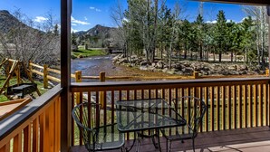 A wooden deck with metal chairs overlooking a river and forested mountains. - Murphy's River Lodge (Estes Park)