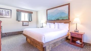 A bedroom with a wooden bed, two bedside tables with lamps, a window with curtains, and a painting on the wall.