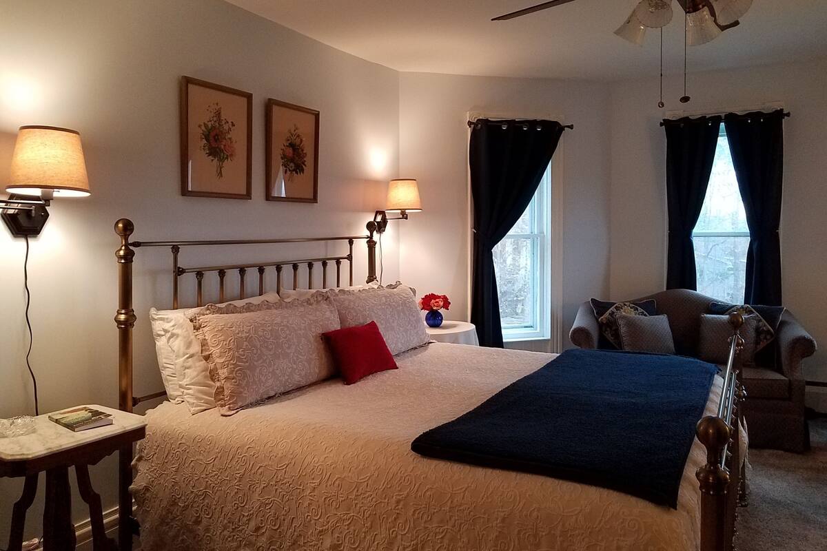 A bedroom with a bed, two wall-mounted lamps, a ceiling fan, and two windows with curtains.
