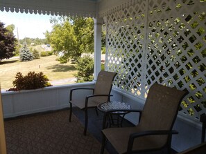 A covered porch with two chairs and a small table, overlooking a grassy area with trees and a building in the distance. - The Fox and the Grapes Bed & Breakfast (Lodi)