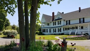 Un grand bâtiment à deux étages, à l’extérieur blanc et au toit gris, entouré de jardins et d’arbres bien entretenus.