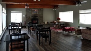 Une pièce spacieuse dotée d’une cheminée, d’un plafond en bois et d’un coin repas avec des chaises et des tables.