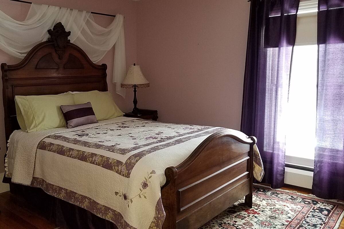 A bedroom with a wooden bed, a nightstand, a lamp, and a window with curtains.