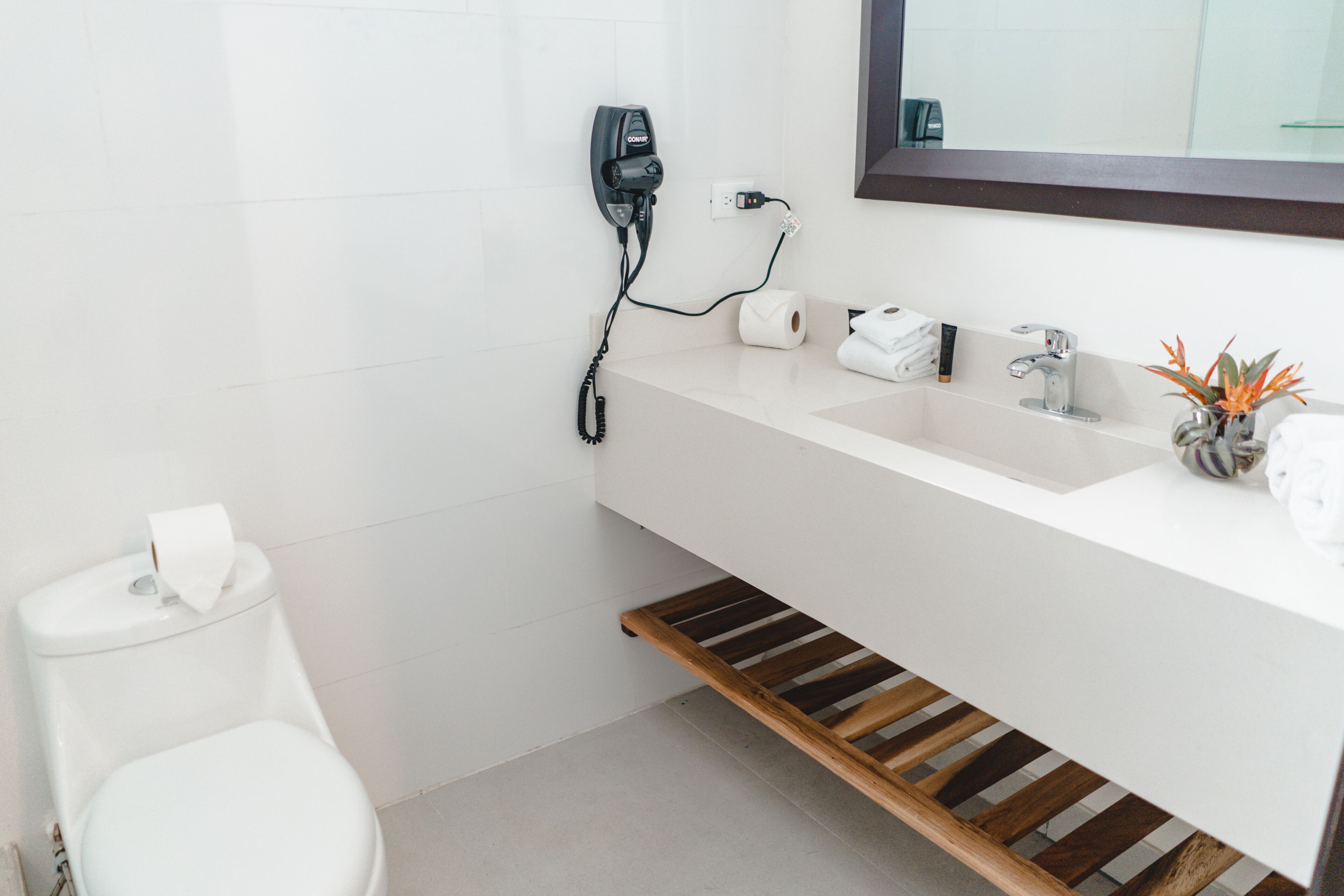 A modern bathroom with a white sink, a mirror, a toilet, and a wooden shelf under the sink.