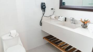 A modern bathroom with a white sink, a mirror, a toilet, and a wooden shelf under the sink.