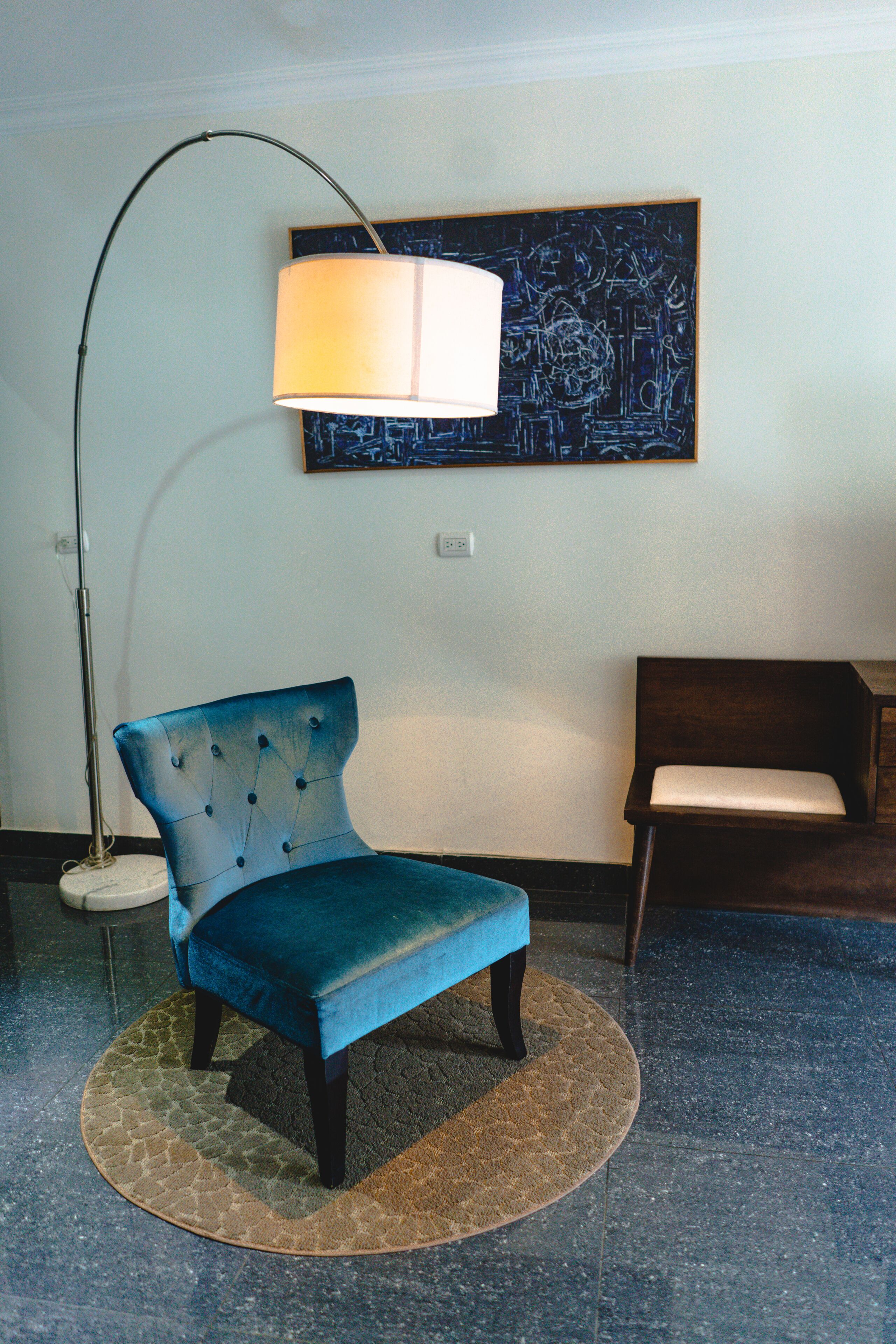 Een blauwe fauteuil met een rond tapijt, een vloerlamp en een schilderij aan de muur.