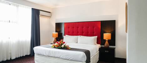 Habitación de hotel con una cama grande, dos lámparas de noche, cabecera roja y un arreglo floral sobre la cama.