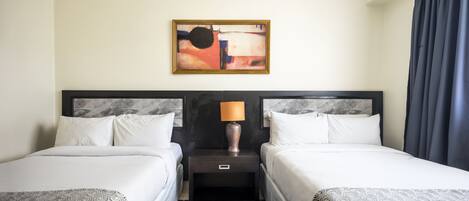 A hotel room with two beds, a nightstand with a lamp, a painting on the wall, and a patterned carpet.