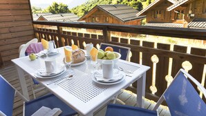 A wooden deck with a table set for breakfast, overlooking a mountainous landscape. - Résidence Odalys Les Chalets de l'Arvan II (Saint-Sorlin-d'Arves)
