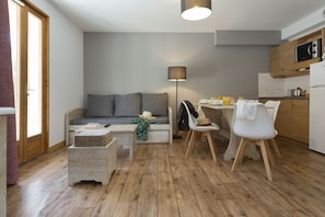 A compact living space with a sofa, dining table, chairs, a lamp, and a kitchen area. - Résidence Odalys Les Chalets de l'Arvan II (Saint-Sorlin-d'Arves)