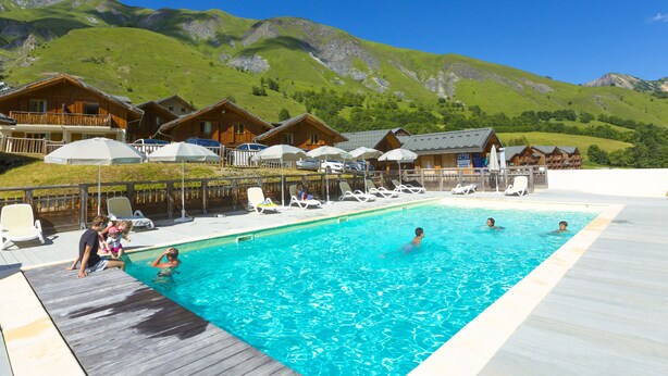 A swimming pool with lounge chairs and wooden cabins in the background. - Résidence Odalys Les Chalets de l'Arvan II (Saint-Sorlin-d'Arves)