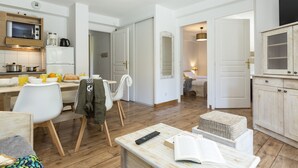 A modern kitchen with a microwave, coffee maker, and refrigerator. There is a dining table with chairs and a bench. A remote control and an open book are on a table. - Résidence Odalys Les Chalets de l'Arvan II (Saint-Sorlin-d'Arves)