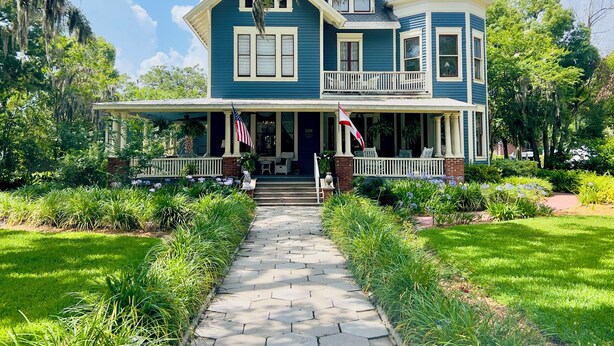 A two-story house with a porch, a flag, and a well-maintained garden. - Hoyt House Amelia Island (Fernandina Beach)