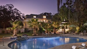 A swimming pool with lounge chairs and a gazebo, surrounded by palm trees and a large house in the background. - Hoyt House Amelia Island (Fernandina Beach)
