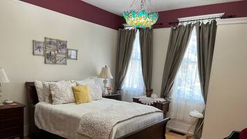A neatly arranged bedroom with a large bed, a bedside table with a lamp, a nightstand, and a chair.