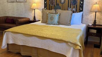 A spacious bedroom with a large bed, two nightstands, a brown leather sofa, and a decorative headboard.