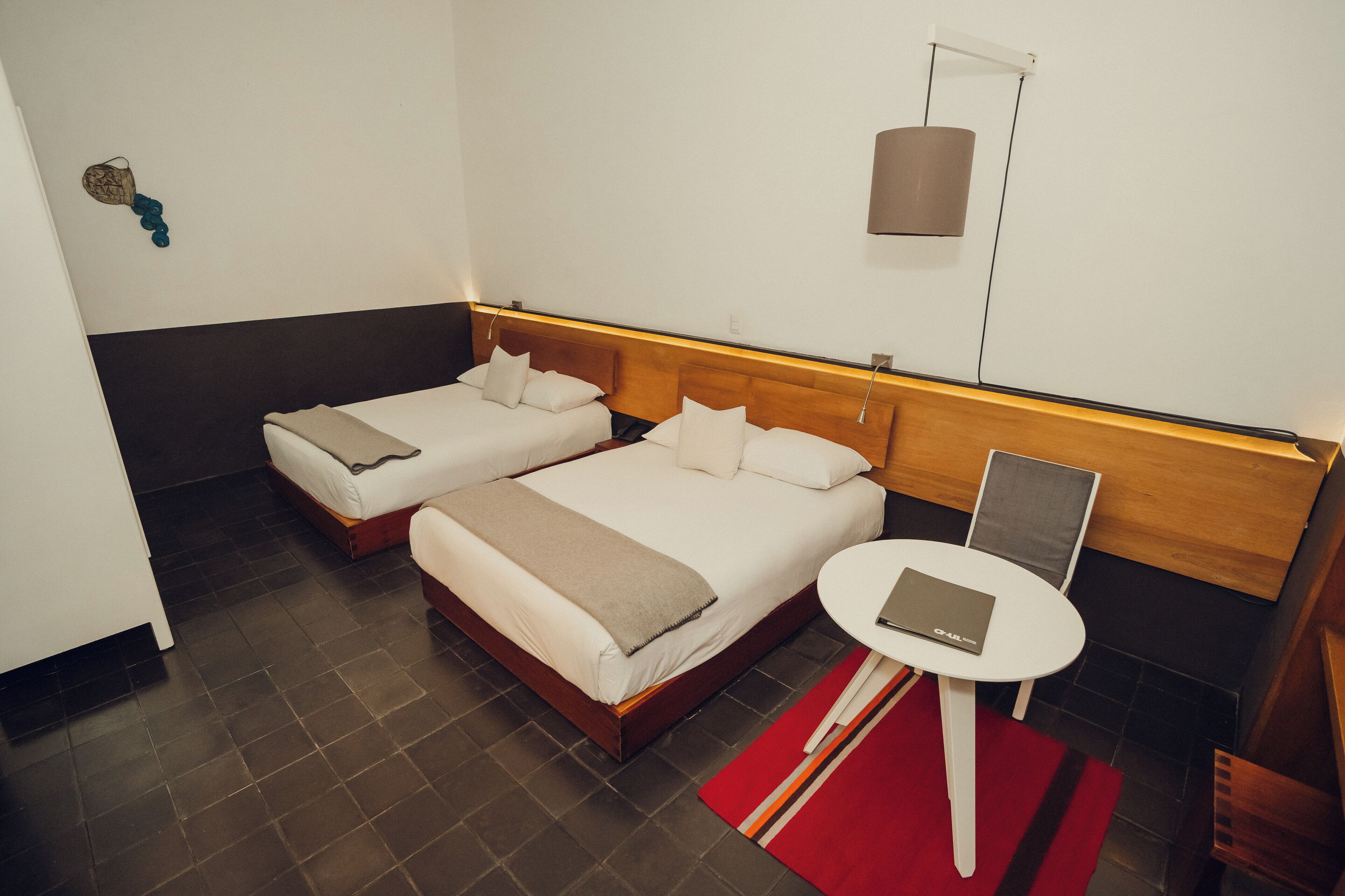 A hotel room with two beds, a small table, and a red rug.