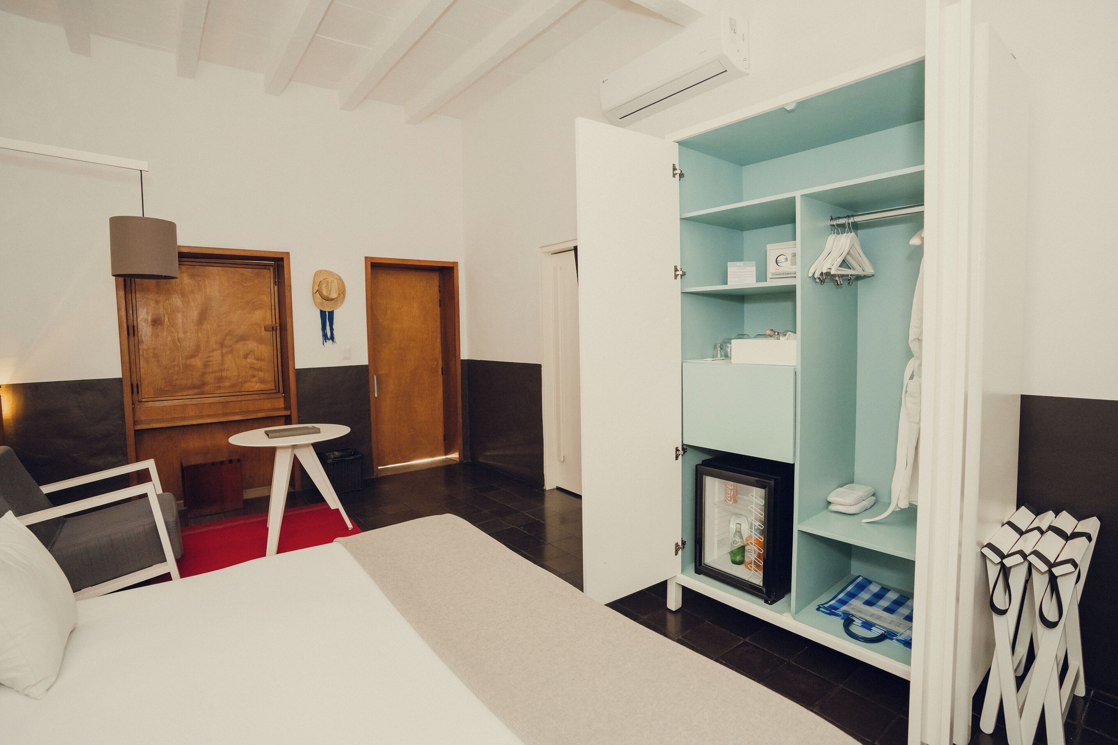 A hotel room with a bed, a small table, a wardrobe, and a red carpet.