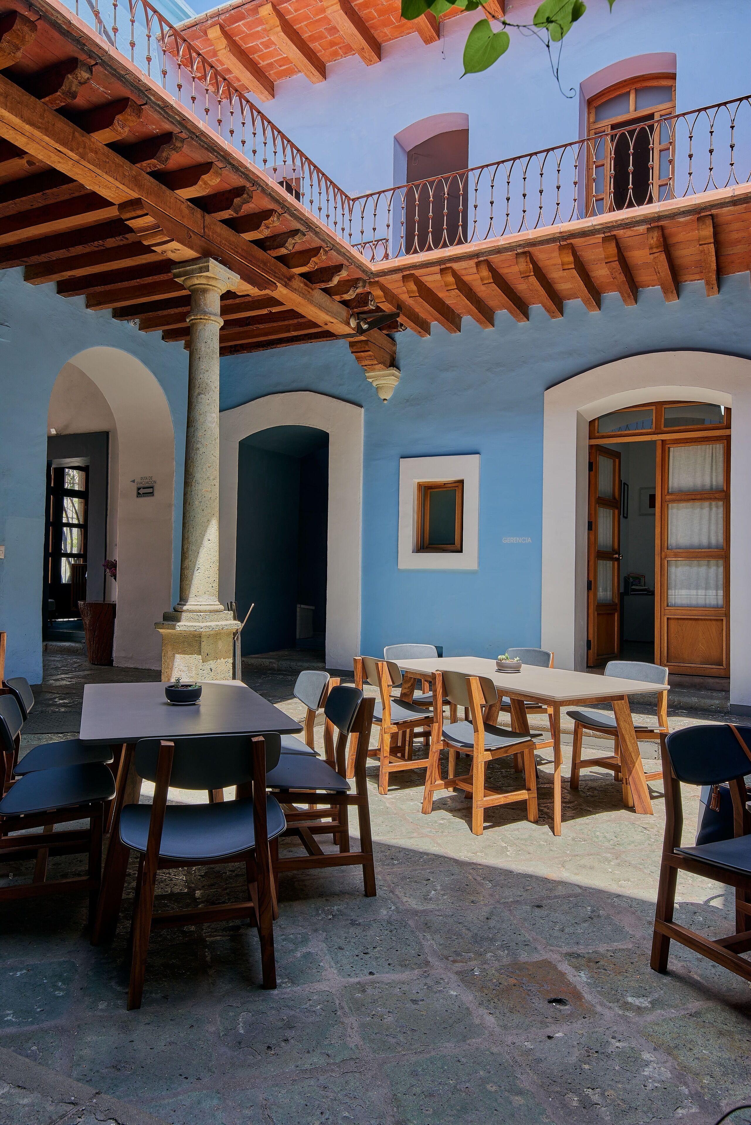 An outdoor patio with wooden tables and chairs, a stone pillar, and a balcony with a railing.