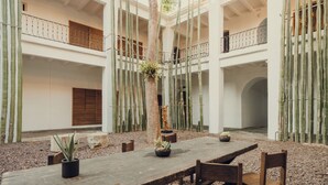 A spacious courtyard with a wooden table and chairs, surrounded by tall bamboo plants and a statue.