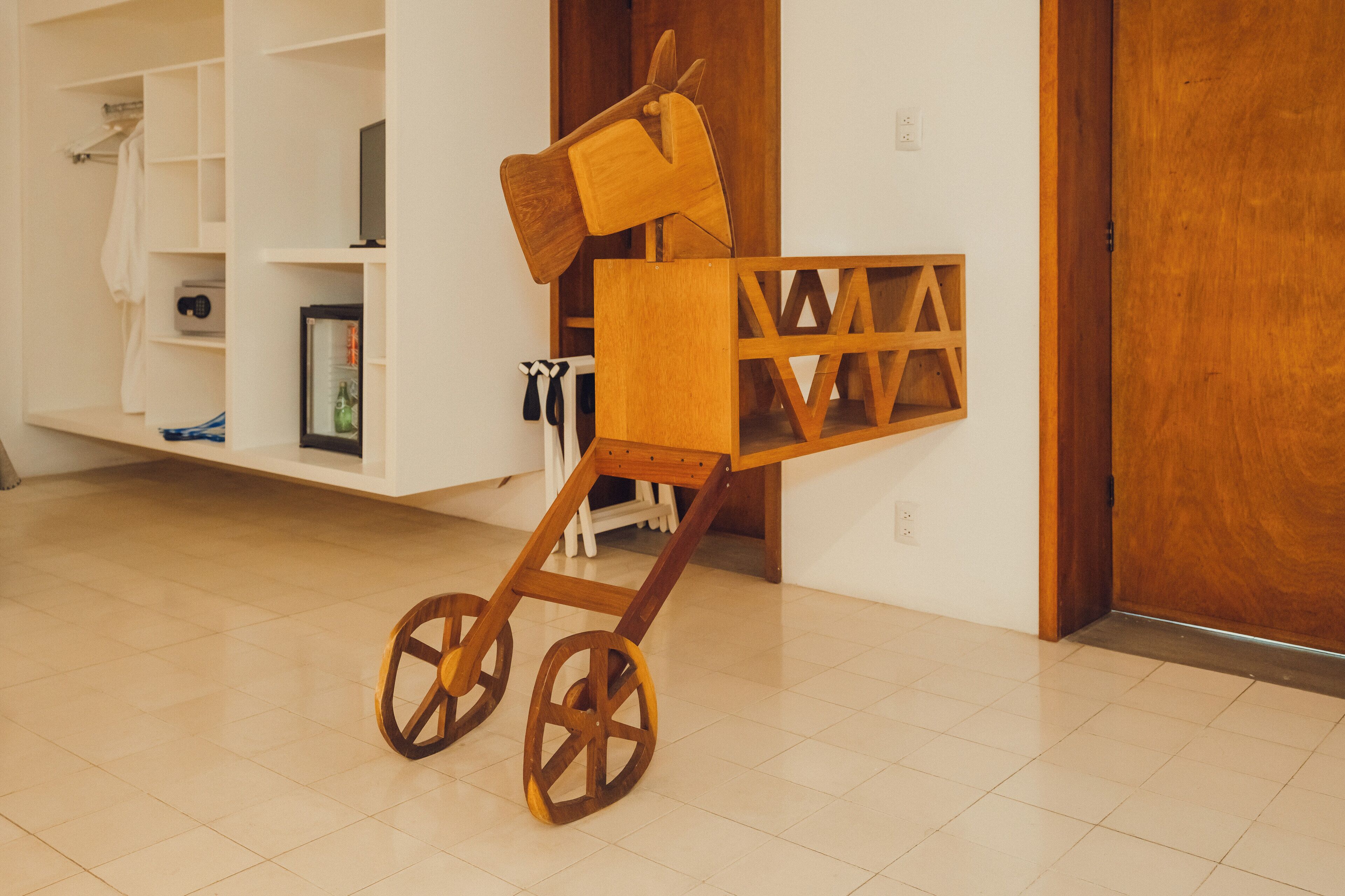 A wooden baby stroller with large wheels, placed in a room with white walls and a wooden door.