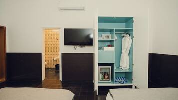 A hotel room with a bed, a TV mounted on the wall, a wardrobe with shelves, and a small refrigerator.