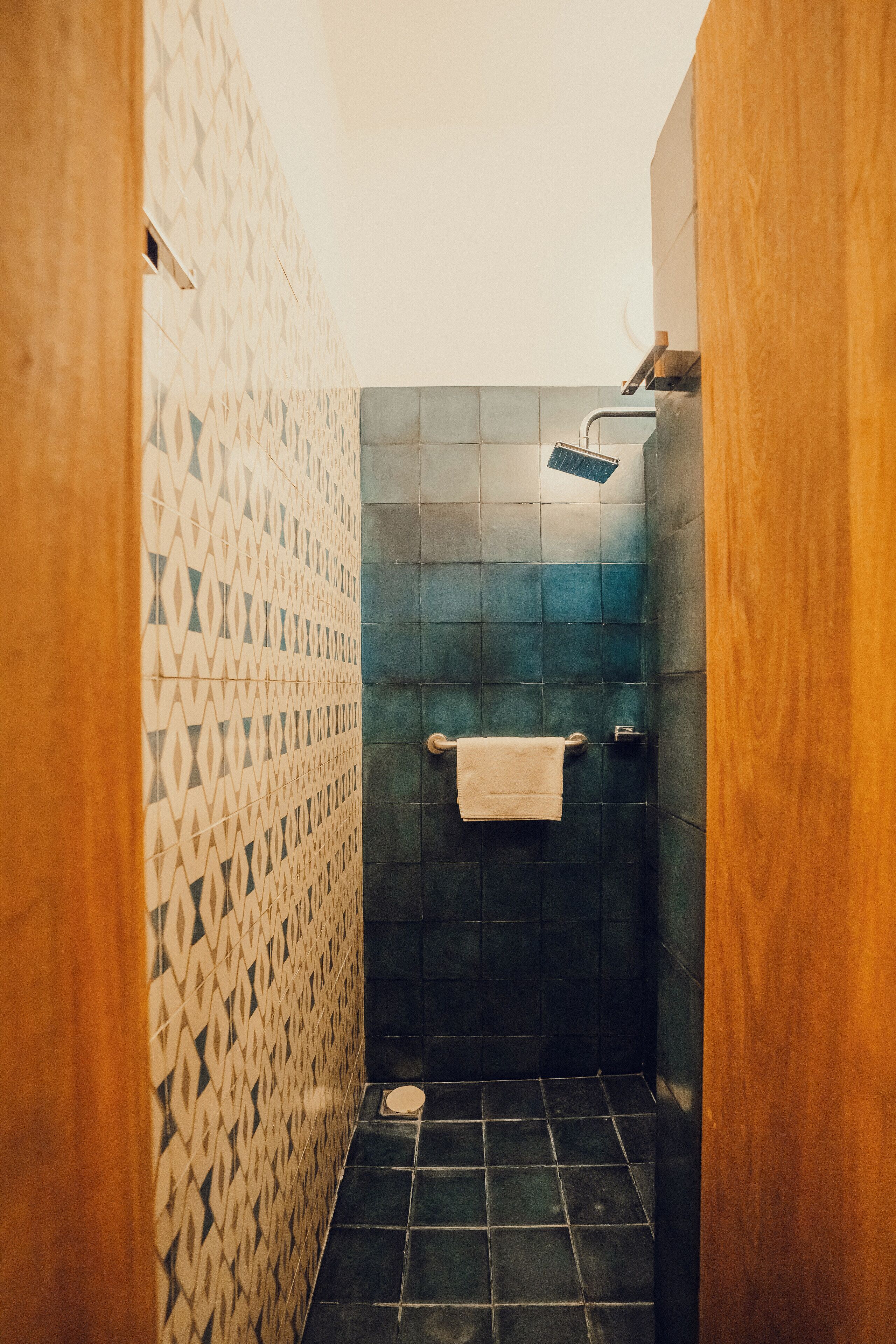 A small, narrow bathroom with patterned tiles on the walls, a dark floor, and a towel hanging on a rack.