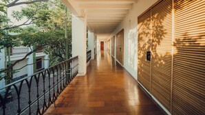A corridor with a tiled floor, wooden shutters, and a metal railing.