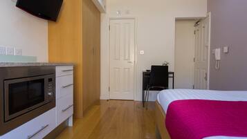 A bedroom with a bed, a desk, a chair, a microwave, and a TV mounted on the wall.