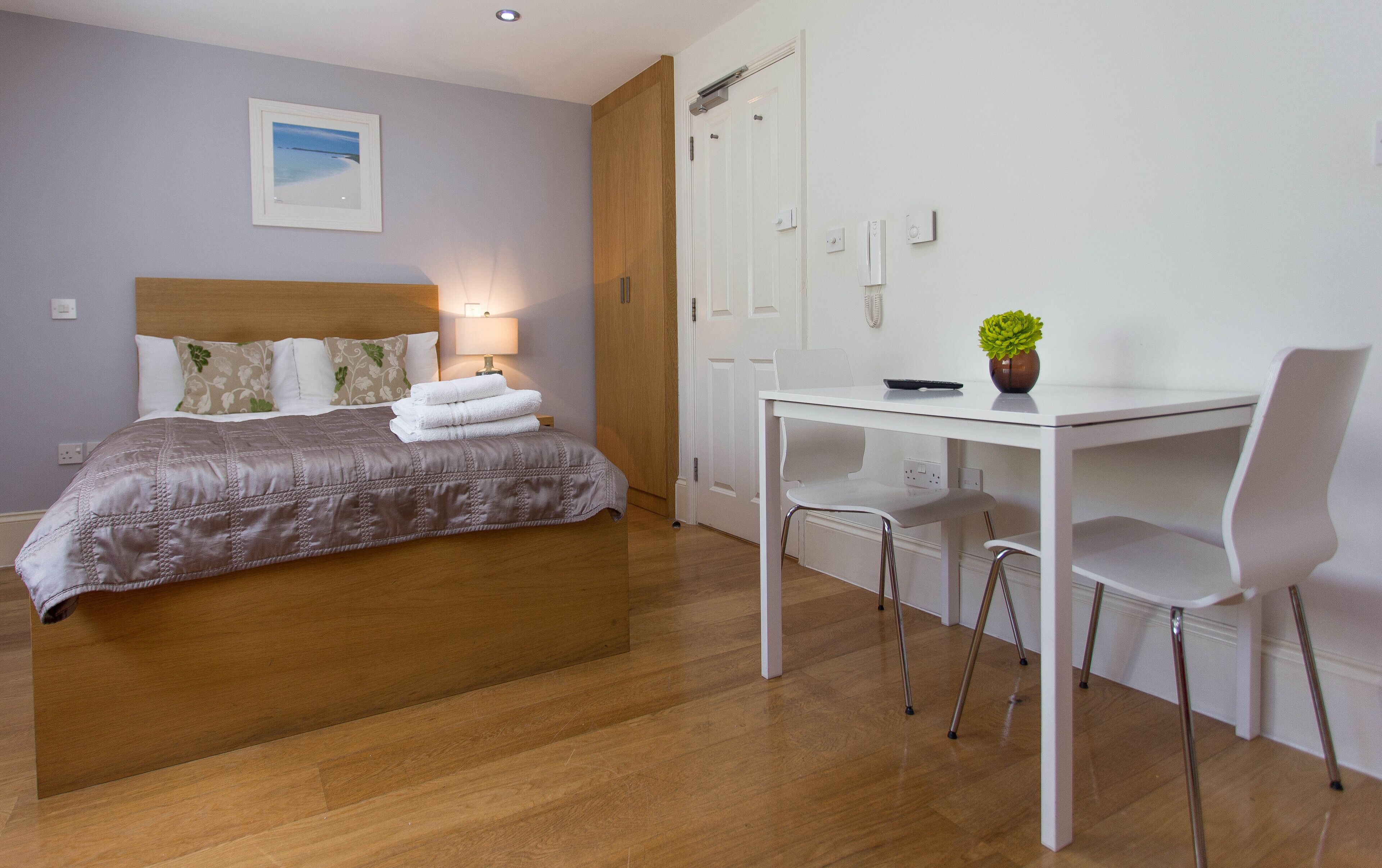 Ein Hotelzimmer mit Bett, Nachttisch, Lampe und Schreibtisch mit Stühlen.