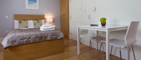 Una camera d'albergo con un letto, un comodino, una lampada e una scrivania con sedie.
