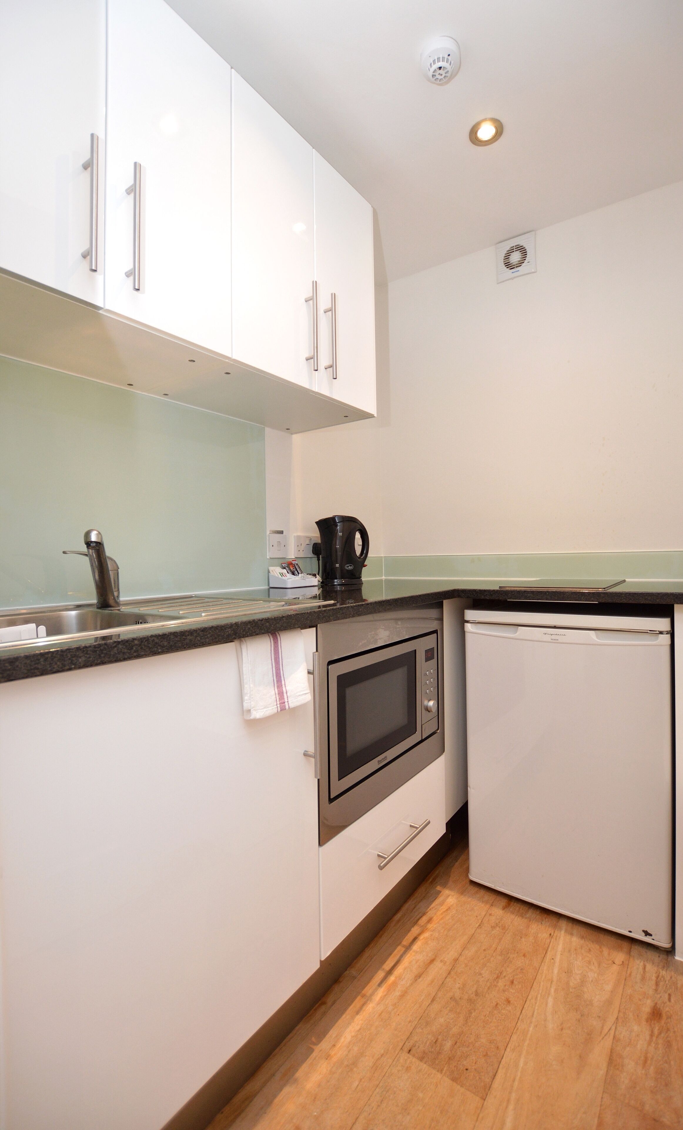 A compact kitchen with white cabinets, a microwave, a coffee maker, and a small refrigerator.