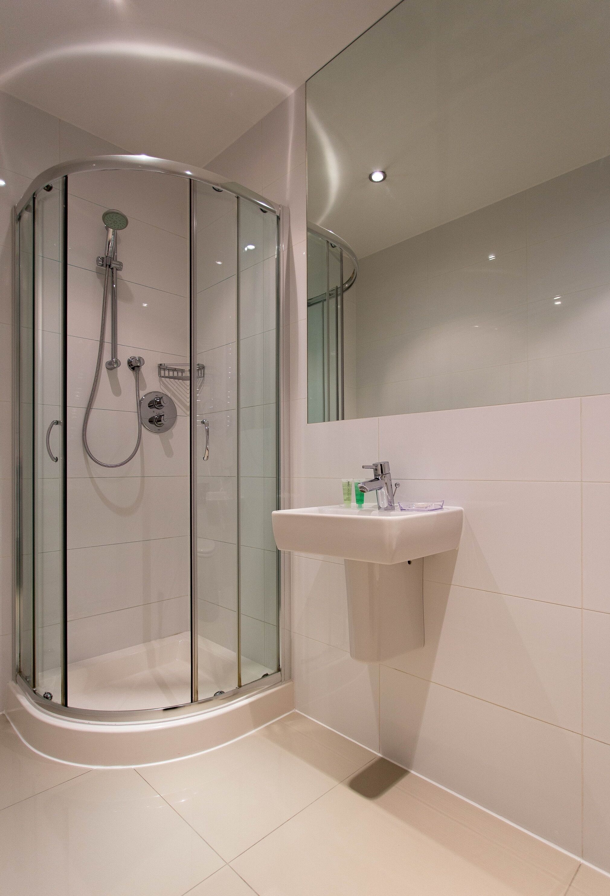 A modern bathroom with a glass-enclosed shower, a white sink, and a large mirror.