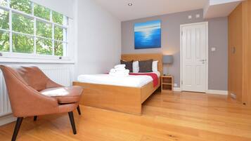 A bedroom with a bed, a chair, a nightstand, a lamp, and a painting on the wall.